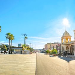 Breite Promenade in Viareggio mit hohen Palmen links und eleganten historischen Gebäuden mit verzierten Türmen rechts unter blauem Himmel.