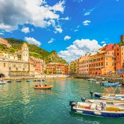 Bunte Häuser umgeben den kleinen Hafen von Vernazza in Cinque Terre mit Fischerbooten im klaren Wasser unter blauem Himmel.
