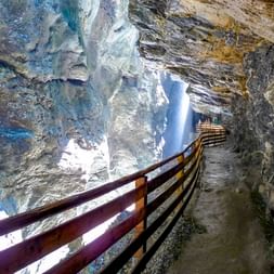 Holzsteg mit Geländer in der Liechtensteinklamm im Pongau. Wasserfall stürzt durch enge Felswände mit dramatischer Beleuchtung.