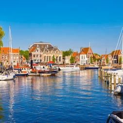 Alter Hafen von Enkhuizen mit Segelbooten und historischen niederländischen Gebäuden mit orangen Dächern unter blauem Himmel.