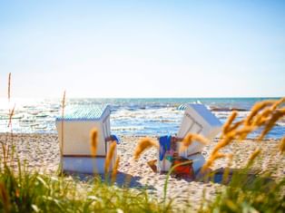 Weiße Strandkörbe am Sandstrand in Bansin, Usedom. Ostseewellen im Hintergrund, Strandgras im Vordergrund.