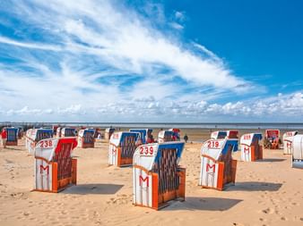 Nummerierte Strandkörbe am Sandstrand in Cuxhaven an der Nordseeküste unter blauem Himmel mit weißen Wolken.