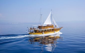 Traditionelles Holzsegelschiff MS Planka mit weißen Segeln auf ruhigem blauen Adriatischen Meer mit sichtbarer Küstenlinie.