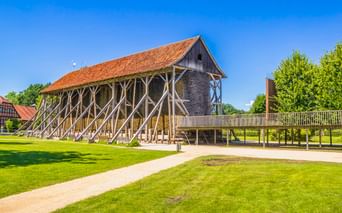 Historisches Salzlagerhaus Saline Gottesgabe in Rheine mit markanten diagonalen Holzstützen und orangefarbenem Ziegeldach auf grüner Wiese.