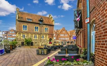 Sonniger Stadtplatz in Meppen mit historischem Rathaus aus gelbem Backstein, Außengastronomie mit Blumenkästen und traditionellen Gebäuden.