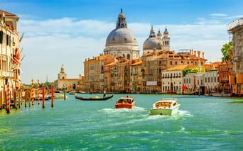 Boote auf dem Canal Grande in Venedig mit den Kuppeln der Basilika Santa Maria della Salute im Hintergrund. Historische Gebäude säumen den Kanal.