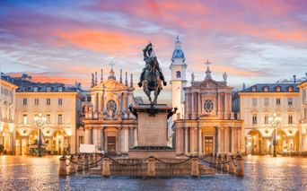 Reiterstandbild in der Mitte der Piazza San Carlo in Turin bei Sonnenuntergang, flankiert von barocken Zwillingskirchen und eleganten Gebäuden.