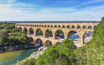 Pont du Gard, antikes römisches Aquädukt mit drei Bogenreihen über einem Flusstal, umgeben von grünen Bäumen unter blauem Himmel.