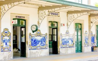 Fassade des Bahnhofs Pinhão mit grünen Türen und Fenstern, geschmückt mit traditionellen portugiesischen blau-weißen Azulejo-Kacheln.