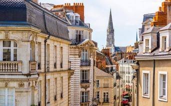 Blick auf historische französische Architektur in Nantes mit cremefarbenen Gebäuden, Schieferdächern und einem Kirchturm im Hintergrund.