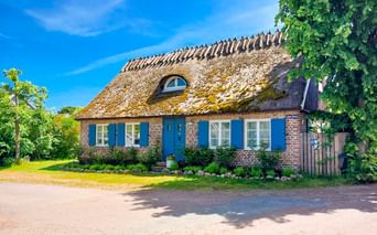 Rotes Backsteinhaus mit Reetdach und blauen Fensterläden auf der Insel Ven, Schweden. Das traditionelle Gebäude hat eine Dachgaube und ist von grünem Rasen umgeben.