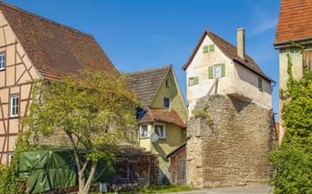 Historischer Lindleinturm aus Stein mit weißem Oberteil und grünen Fensterläden in Creglingen, umgeben von traditionellen Fachwerkhäusern.