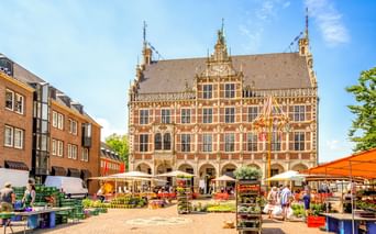 Prachtvolles Renaissance-Rathaus in Bocholt mit Arkadengang im Erdgeschoss und dekorativer Fassade. Marktstände mit orangen Markisen füllen den Platz.