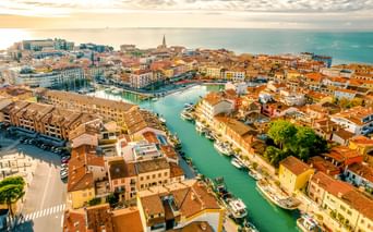 Luftaufnahme von Grado, Italien mit bunten Gebäuden und Terrakottadächern entlang eines Kanals zur Adria bei Sonnenuntergang.