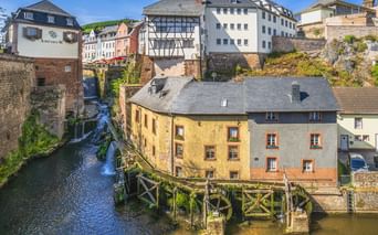 Wasserfall, der durch historische Gebäude in Saarburg fließt. Traditionelle Fachwerkhäuser und Steinbauten umgeben den Wasserlauf.