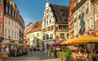 Fußgängerzone in Kitzingens Altstadt mit bunten Fachwerkhäusern, Straßencafés mit gelben Sonnenschirmen und Marktständen.