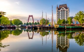 Historische Schiffe im Alten Hafen von Rotterdam mit ruhigen Wasserspiegelungen. Das Witte Huis und die Willemsbrücke sind im Hintergrund sichtbar.
