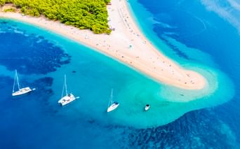 Luftaufnahme vom Strand Zlatni Rat in Bol mit weißer Sandzunge im türkisfarbenen Adriatischen Meer, Segelbooten und grünem Wald.