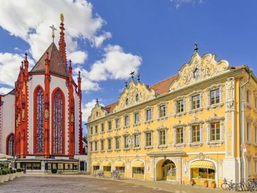 Rot-weiße gotische Marienkapelle neben dem gelben Rokoko-Gebäude Haus zum Falken am Marktplatz in Würzburg unter blauem Himmel.