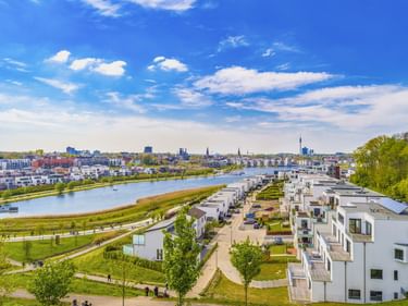 Luftaufnahme des Phoenix Sees in Dortmund mit modernen weißen Wohngebäuden, grünen Parkanlagen und Stadtsilhouette unter blauem Himmel.