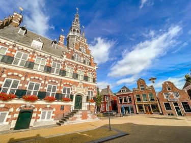 Renaissance-Rathaus in Franeker mit rot-weißer Backsteinfassade, verziertem Turm und Blumenkästen. Traditionelle niederländische Häuser säumen den Platz.
