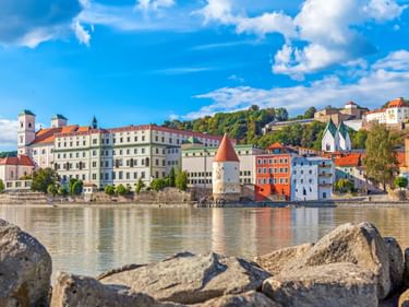Bunte historische Gebäude der Passauer Altstadt an der Donau mit weißem Turm mit rotem Dach und Kirchtürmen unter blauem Himmel.
