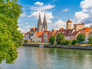 Blick auf Regensburgs historische Altstadt mit dem Dom und mittelalterlichem Brückenturm an der Donau unter blauem Himmel.