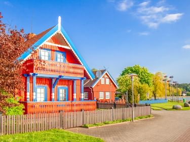 Rotes Holzhaus mit blauem Zierrat und Balkonen in Nida. Die traditionelle baltische Architektur zeigt verzierte Giebel unter klarem Himmel.