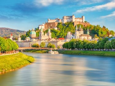 Festung Hohensalzburg auf einem Hügel über Salzburgs Altstadt mit barocken Kirchen und der Salzach im Vordergrund.