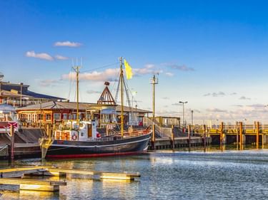 Traditionelle Fischerboote im Hafen von List auf Sylt mit Holzstegen und Hafengebäuden unter blauem Himmel mit vereinzelten Wolken.