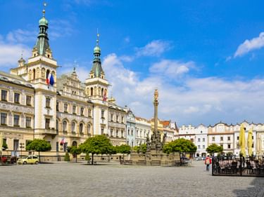 Stadtplatz von Pardubice mit prächtigem Rathaus mit grünen Türmen, barocker Säule und bunten historischen Gebäuden unter blauem Himmel.