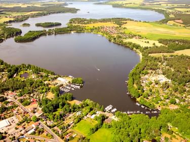 Luftaufnahme vom Schwielochsee mit bewaldeten Inseln, umliegenden Dörfern, landwirtschaftlichen Feldern und Bootshäfen entlang der Ufer.