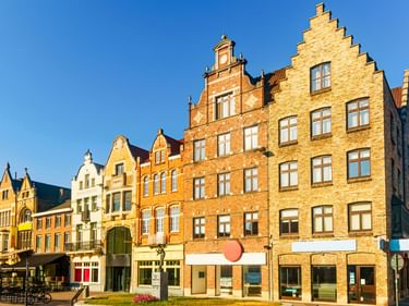 Reihe traditioneller flämischer Treppengiebelhäuser in Roeselare mit Backsteinfassaden in Gelb- und Orangetönen unter blauem Himmel.