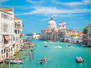 Venedigs Canal Grande mit türkisfarbenem Wasser, Booten und bunten Gebäuden. Die weiße Kuppel der Basilika Santa Maria della Salute prägt die Skyline.