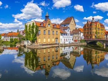 Bunte historische Gebäude entlang der Weser in Eschwege mit einer Steinbrücke. Die Gebäude und der blaue Himmel spiegeln sich im ruhigen Wasser.
