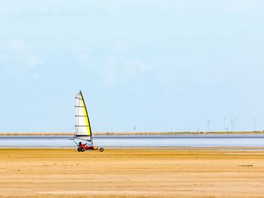 Strandsegler mit gelbem Segel auf breitem Sandstrand der Insel Rømø. Blauer Himmel darüber, Wasser und Dünen im Hintergrund sichtbar.
