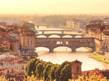 Panoramablick auf Florenz mit mehreren Brücken über den Arno, darunter die Ponte Vecchio, mit historischen Gebäuden im goldenen Abendlicht.