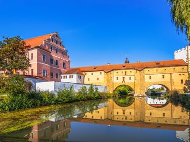 Historisches Stadtbrille Wassertor mit zwei Bögen spiegelt sich im ruhigen Wasser in Amberg, mit bunten Gebäuden und orangen Dächern unter blauem Himmel.