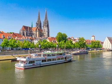 Touristenboot auf der Donau in Regensburg mit dem Regensburger Dom mit seinen zwei Türmen, der die historische Skyline dominiert.