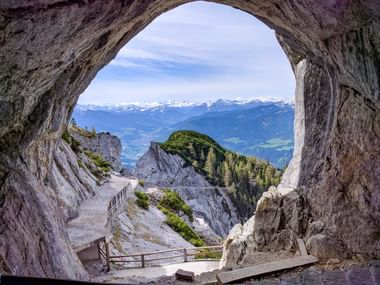 Blick aus der Eisriesenwelt-Höhle bei Werfen mit natürlichem Felsbogen, der schneebedeckte Berge und grüne Täler einrahmt.