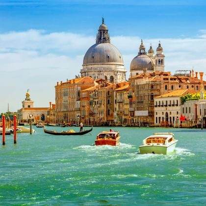 Boote und Gondel auf dem Canale Grande in Venedig mit der ikonischen Kuppel der Basilika Santa Maria della Salute und historischen Gebäuden.
