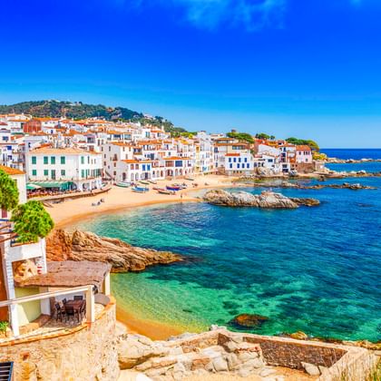 Calella de Palafrugell: weiße Häuser mit Terrakottadächern entlang Sandstränden und türkisfarbenem Mittelmeer mit Felsformationen.