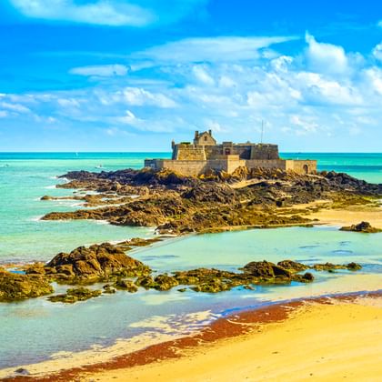 Festung Fort National auf felsiger Insel bei Ebbe in Saint-Malo, umgeben von türkisfarbenem Wasser, Sandstrand und freiliegenden Felsen.