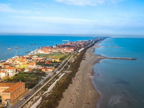 Luftaufnahme von Pellestrina, einer schmalen Insel mit bunten Gebäuden entlang einer Küstenstraße zwischen der Adria und der Lagune von Venedig.