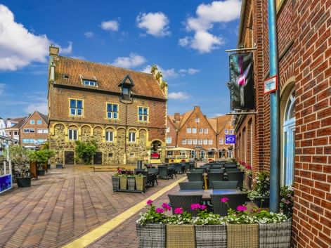 Sonniger Stadtplatz in Meppen mit historischem Rathaus aus gelbem Backstein, Außengastronomie mit Blumenkästen und traditionellen Gebäuden.