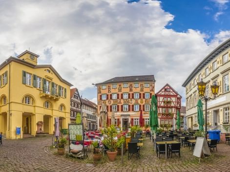 Kopfsteinpflaster-Marktplatz in Eberbach mit bunten Fachwerkhäusern, Außengastronomie und gelbem Rathaus unter bewölktem Himmel.