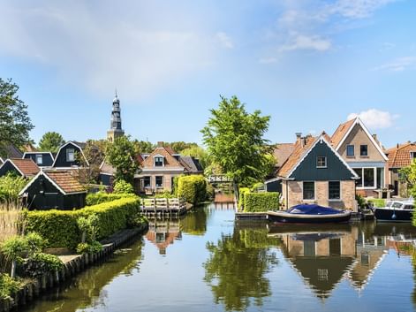 Ruhiger Kanal in Hindeloopen mit traditionellen niederländischen Häusern, roten Ziegeldächern und Booten am Ufer. Ein Kirchturm erhebt sich im Hintergrund.