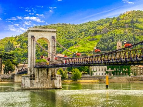 Passerelle Marc Seguin Hängebrücke über die Rhône in Tournon mit grünen Weinbergen und historischen Gebäuden im Hintergrund.