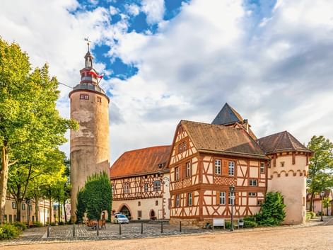 Historische Schlossanlage in Tauberbischofsheim mit rundem Steinturm, Fachwerkhäusern und Kopfsteinpflaster unter blauem Himmel.