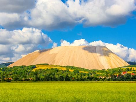 Großer weißer Salzberg Monte Kali erhebt sich über grüne Felder und Dorfhäuser in Heringen an der Werra unter blauem Himmel mit weißen Wolken.